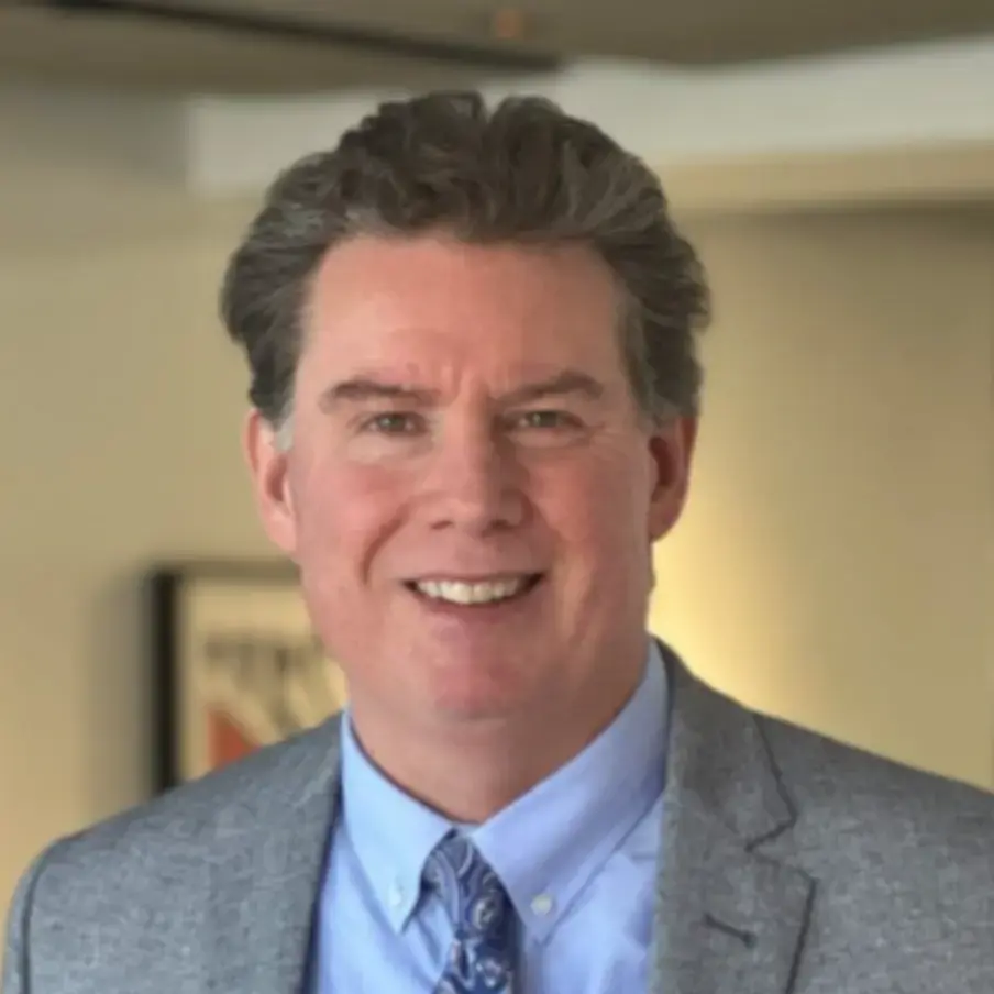 Professional head-and-shoulders portrait of a smiling man in a gray suit and blue shirt.